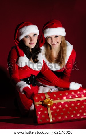 two girl in Santa costume opening christmas gift. on red