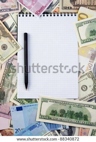 Opened spiral notepad (notebook) sheet in a cage on money background ( euro and dollars cash).   with black pen