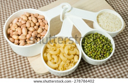 Foods High in Carbohydrate, Raw Pasta, Rice, Peanuts and Mung Beans in Plastic Measuring Spoons.