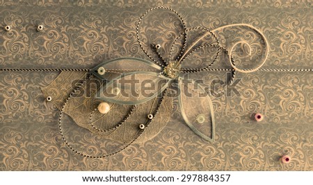 Bronze horizontal handmade greeting decoration with shiny beads, embroidery, silver thread in form of flower and butterfly on background of vintage fabric
