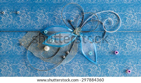 Blue horizontal handmade greeting decoration with shiny beads, embroidery, silver thread in form of flower and butterfly on background of vintage fabric