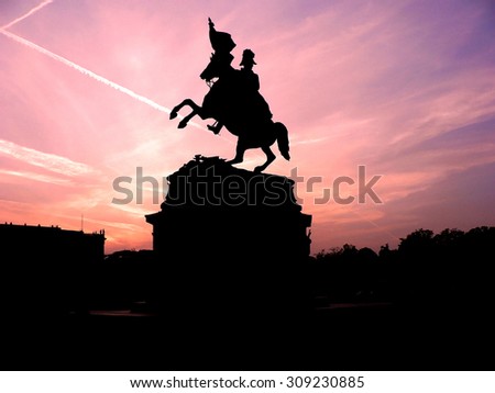 Black silhouette of monument of horse rider with flag on background of rose violet sunset