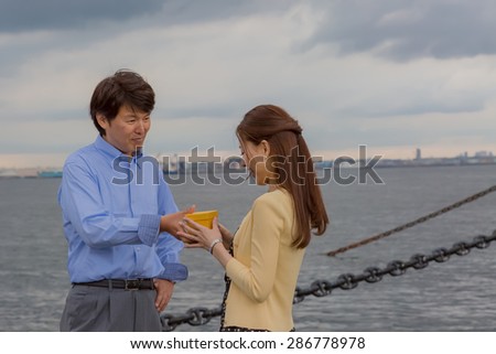 A Japanese man giving a present to a girl friend at a wharf