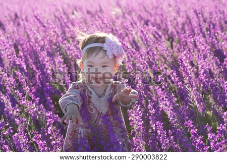 Little funny baby girl smiling in a purple flowers field