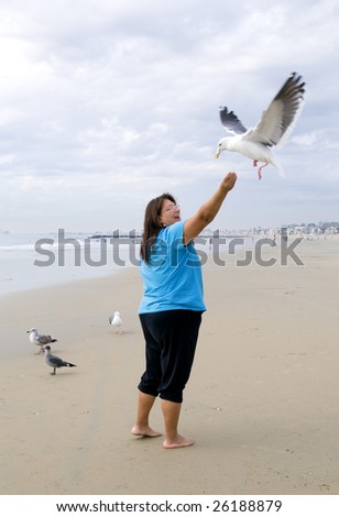 Smiling lady enjoys feeding the birds. She holds pieces of bread in the air and the birds fly by and grab it out of her hand.