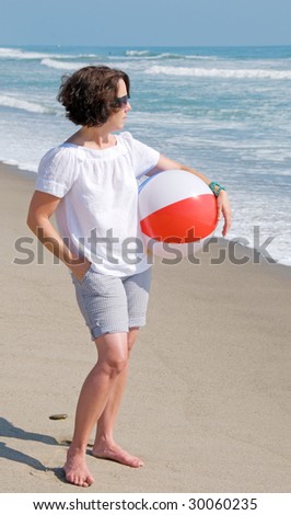 Woman holding a beach ball and looking out at the ocean