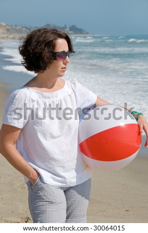 Young woman carrying bright beach ball and looking at the ocean