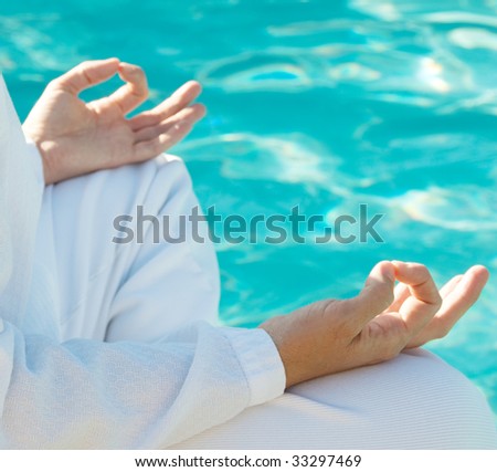 Hands in meditation mudra above water, shallow depth of field, focus on front hand