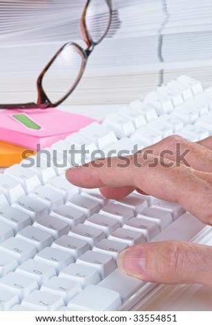 Computer keyboard on desk with folders and work related items, shallow depth of field, focus on first finger