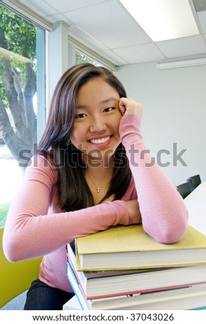 Student teen girl in classroom leaning on stack of books