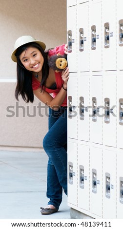 Beautiful teenage girl hiding behind the school lockers wearing a safari hat and carrying her stuffed monkey. Concept is Adventure In High School.