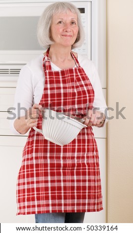 Senior woman smiling in her kitchen and holding cooking tools