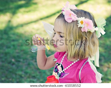 Young girl of 4 years wearing fairy wings and blowing bubbles in the park.