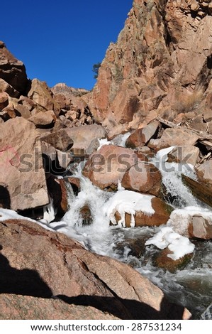 Mountain Stream falling over reddish icy rocks in the mountains near Jemez Springs, New Mexico.  Note the Ice Wolf on the rocks.  Vertical orientation with blue sky intensified using polarizing filter