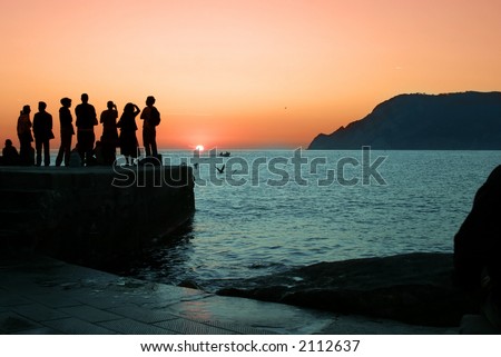 Silhouette of a group of people watching the sunset on the Cinque Terre coast area of Italy.