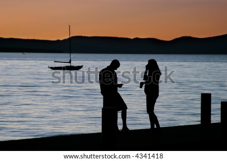 Man, woman and small sailboat at lake with beautiful sunset.