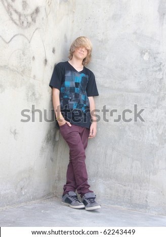 stock photo Cute teen boy with long shaggy hair standing against a cement 