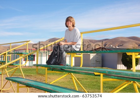 Cute smiling teen boy sitting a the top of school bleachers.