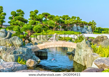 Cypresses emerge to stone bridge garden architecture in Vietnam with rockery stone, bonsai cypress, pine perpetual, below the swimming pool fishes streams have very beautiful paintings