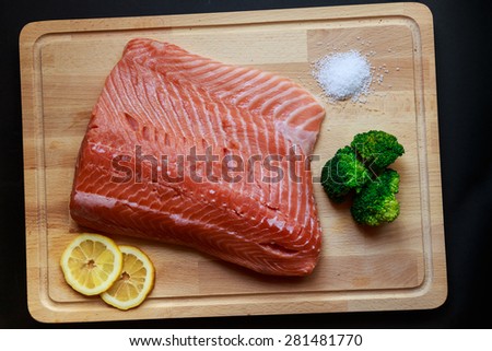 Raw salmon with two lemon slices, broccoli and sea salt on a wooden board.