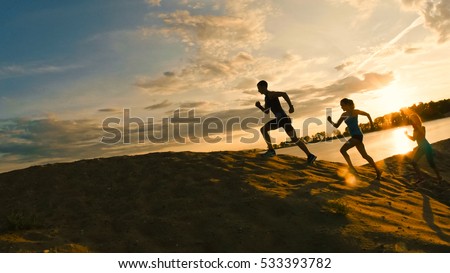 group of athletes - two girls and a guy are fleeing the mountain, near river at dusk