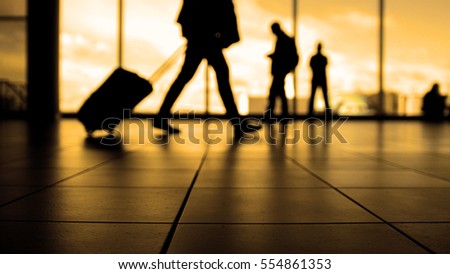 Travellers in airport walking to departures by escalator in front of window, silhouette, warm