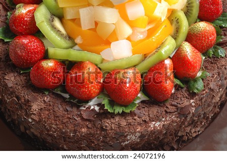 It is a part view of chocolate cake, with lots of fruits, such as strawberries, Kiwi.