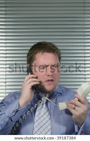 Busy Caucasian Businessman getting stressed using two telephones,