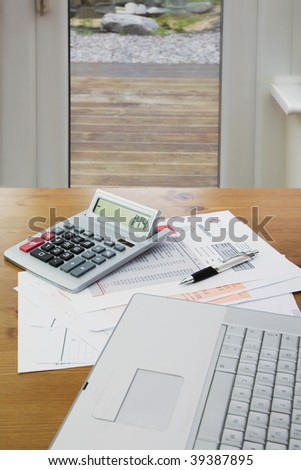 HouseHold Accounting using Calculator,Pen,lap Top and Bank statement and credit card statements on a Wooden Dinning table
