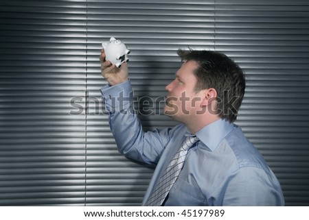 Businessman holding piggy bank and looking to see if there is money inside