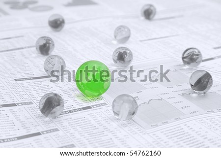 Black and white marbles with a large green marble as the map of the Globe on a News paper  page showing stocks and shares