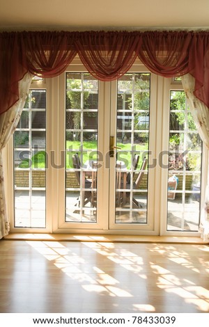 view from a empty room showing curtains and French uPVC patio doors with sun shining through and garden in the background