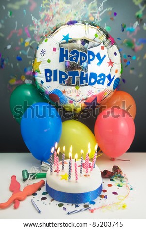 Party concept showing a Birthday cake,candles,balloons,party decorations and confetti coming down from above,