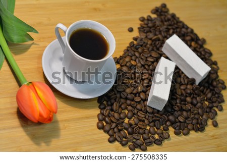 coffee in a cup and coffee beans with a fresh tulip and marshmellow closeup