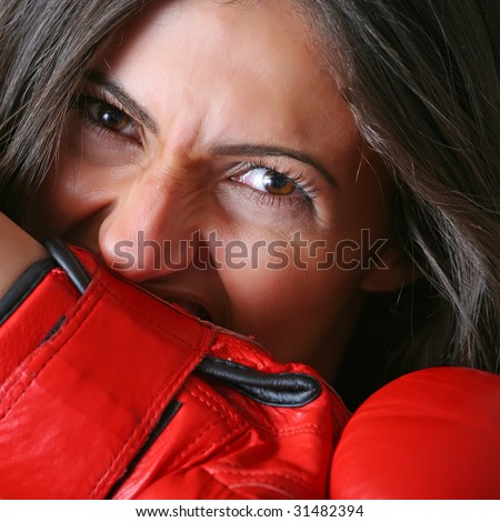 Young woman with black hair pulls together with a teeth from a hand a red boxing glove