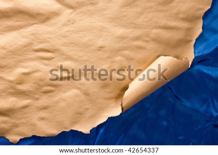 Burnt parchment rolled at corner on wrinkled blue textile