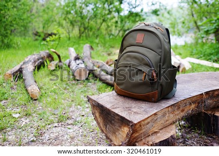 Travel backpack on the wooden bench in the forest. Camping equipment and nature background.