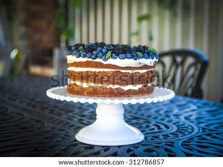 Blueberry and blackberry naked carrot cake with vanilla frosting on a white porcelain cake stand. Natural life.