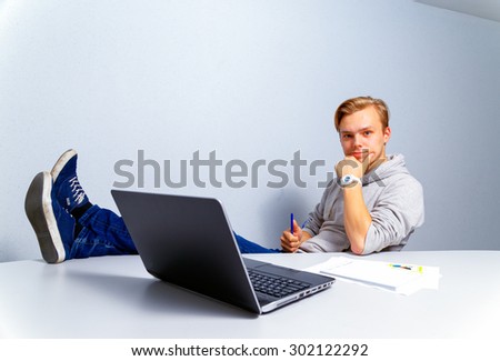 The self-assured businessman in casual clothes at office. Sits at a table in front of the laptop.