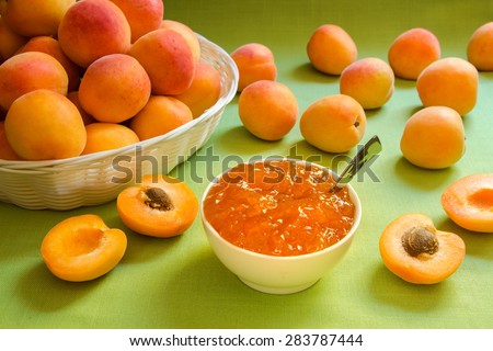 The right side of the frame cup with apricot jam on the left side basket with apricots on a green tablecloth. In the background is blurred apricots. Apricot jam . Horizontal shot.\
Close-up.