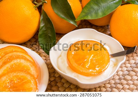 22.	White bowl with yoghurt and one piece of candied orange on located on the right side of the frame on an orange background. Candied oranges and yogurt. Horizontal shot. Close-up.