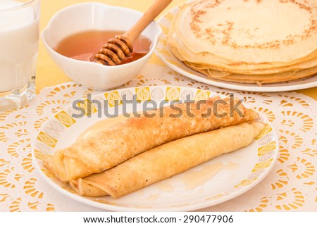 Pancakes rolled in a tube and poured honey on a plate, a glass of milk, a bowl of honey, a plate with a stack of pancakes. Pancakes and honey. Horizontal shot. Close-up.