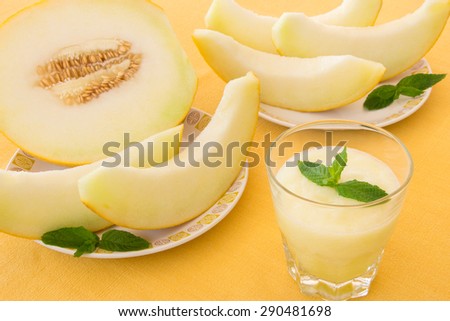 Melon smoothie with mint leafs, cut slices of melon on a yellow tablecloth. Melon smoothie in a glass. Horizontal shot. Close-up.