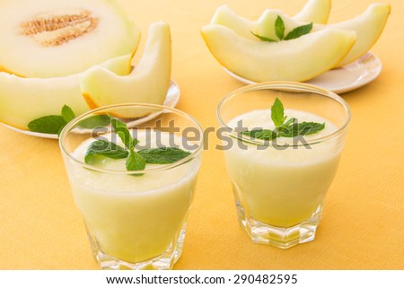 Melon smoothies with mint leaf, cut slices of melon on a yellow tablecloth. 2 Melon smoothies in a glass. Horizontal shot. Close-up.