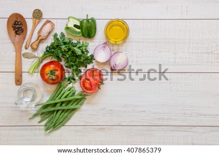 Left fresh vegetables ready to cook tomatoes, peppers, green beans, onions, parsley, spices in wooden spoons on light wood background, right empty space. Vegetables ingredients. Horizontal.Top view.