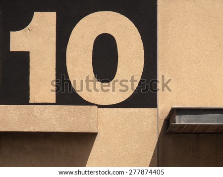 Dark-yellow wall of an industrial building in the port with protruding out of it concrete and iron structural elements, and the image of her black paint serial number in the form of ten