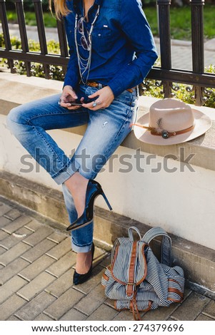 young stylish pretty woman, hands holding a phone, dressed in denim shirt and jeans, high heel shoes, hat, backpack, sunny day, good weather, city street, vacation europe, travel, detail, accessories