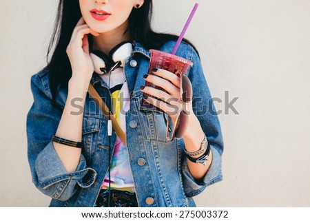 young beautiful happy stylish hipster girl, cocktail, smoozy drink, denim jacket, smiling, fashion, teen, cool accessories, purse, hat, sunglasses, vintage style, wall background, headphones, close up