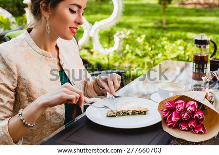 young stylish woman sitting in cafe, eating tasty pie, enjoying healthy food, tulips, happy birthday party, city street, boho outfit, europe vacation, fashion, romantic dinner, smiling