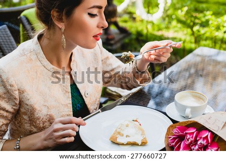 young stylish woman sitting in cafe, eating tasty pie, enjoying healthy food, cappuccino, tulips, happy birthday party, city street, boho outfit, europe vacation, fashion, romantic dinner, open mouth